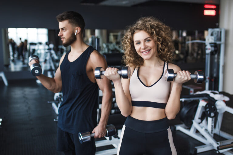 About Beautiful young sporty couple trainer and woman showing muscle and workout in gym during training.